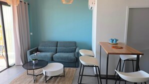 A living area with a sofa, a round table, two white chairs, and a small table with cups. - Loft with sea view, A/C and parking (Saint-Pierre)