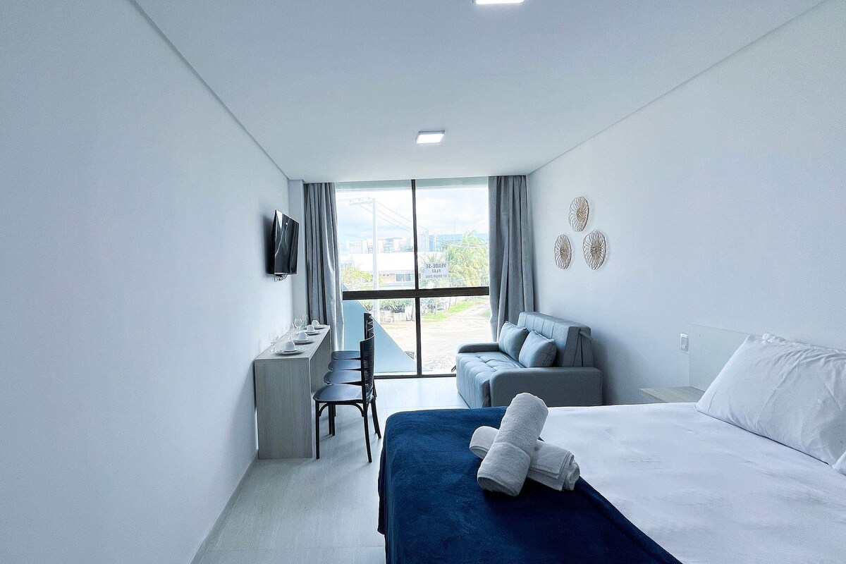 A hotel room with a bed, a desk, a chair, a sofa, and a TV.
