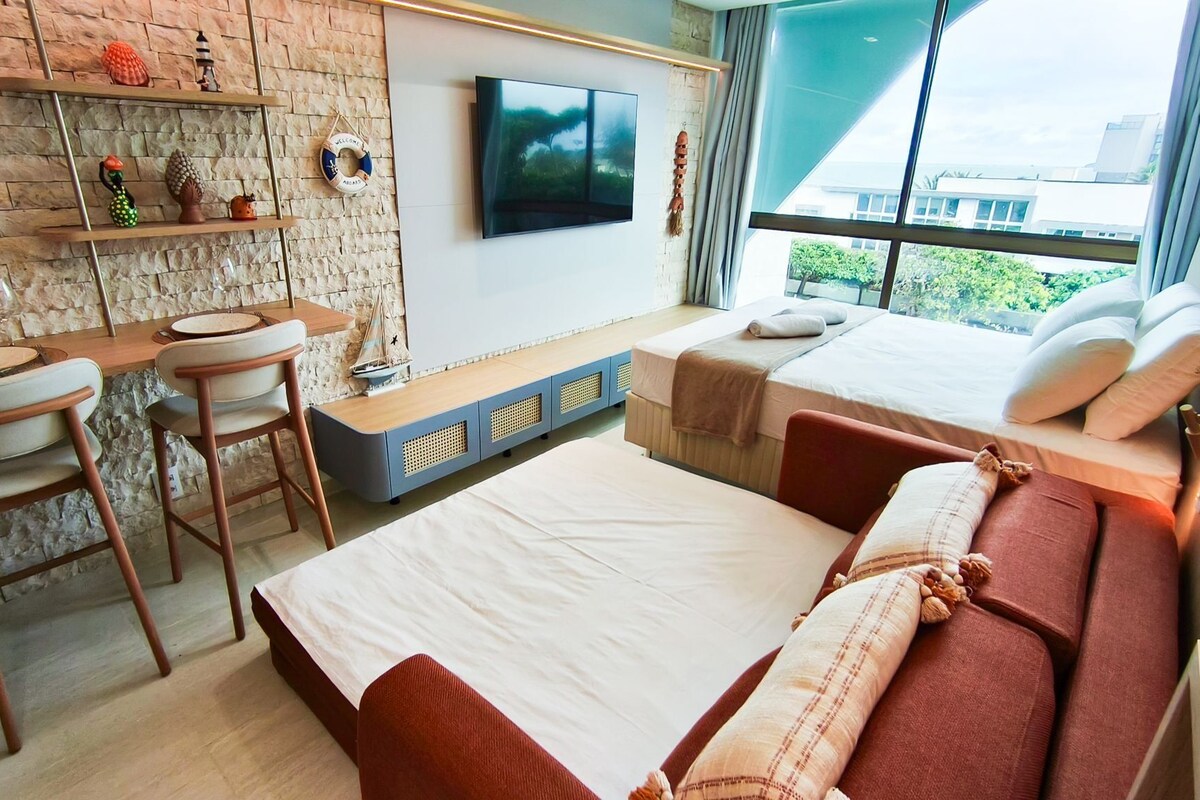 A modern hotel room with a brick wall, a flat-screen TV, a bed with red bedding, a desk with a chair, and a window with a city view.