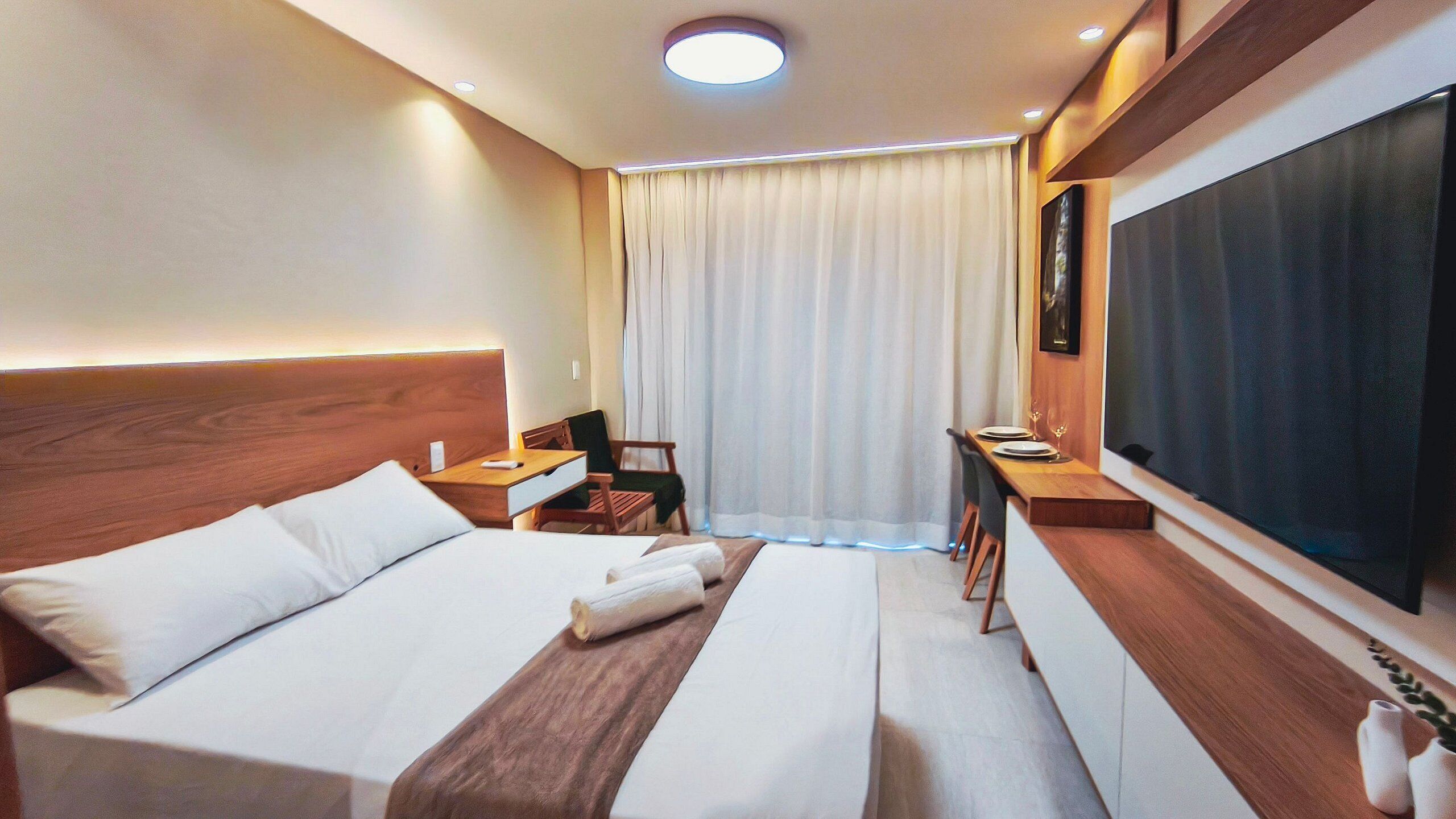Ein Hotelzimmer mit Bett, Nachttischen, Schreibtisch, Stuhl, Fernseher und einem Fenster mit Vorhängen.