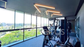 Un gimnasio con equipo de ejercicio y amplias ventanas con vistas a un paisaje urbano.