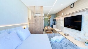 A modern hotel room with a bed, a TV, a dining area, and a bathroom. - Prime Beach Carneiros (Tamandaré)