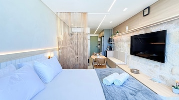 Una habitación de hotel moderna con cama, televisor, zona de comedor y baño.