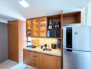 A modern kitchen with wooden cabinets, a stainless steel refrigerator, and various appliances including a coffee maker and microwave. - Prime Beach Carneiros (Tamandaré)