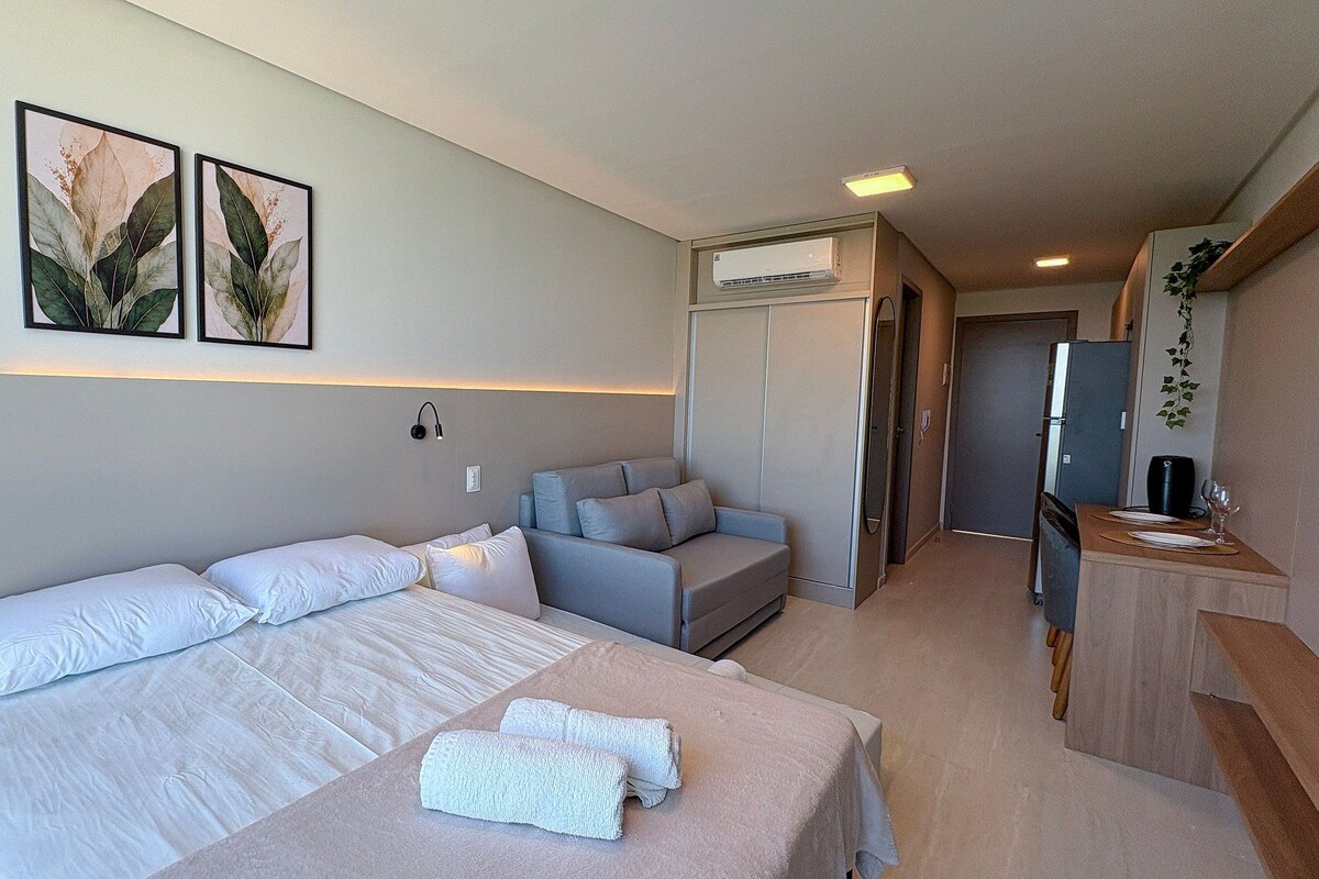 A hotel room with a bed, a sofa, a desk, and a kitchenette.