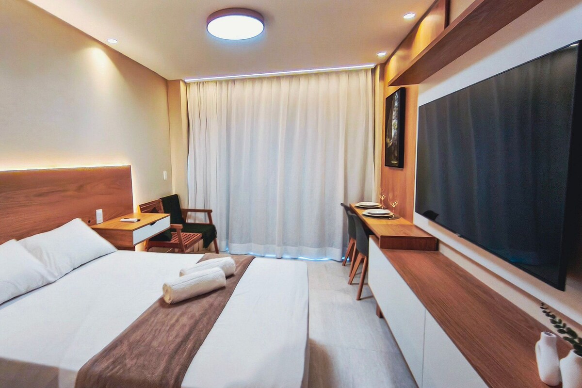 A hotel room with a bed, bedside tables, a desk, a chair, a TV, and a window with curtains.
