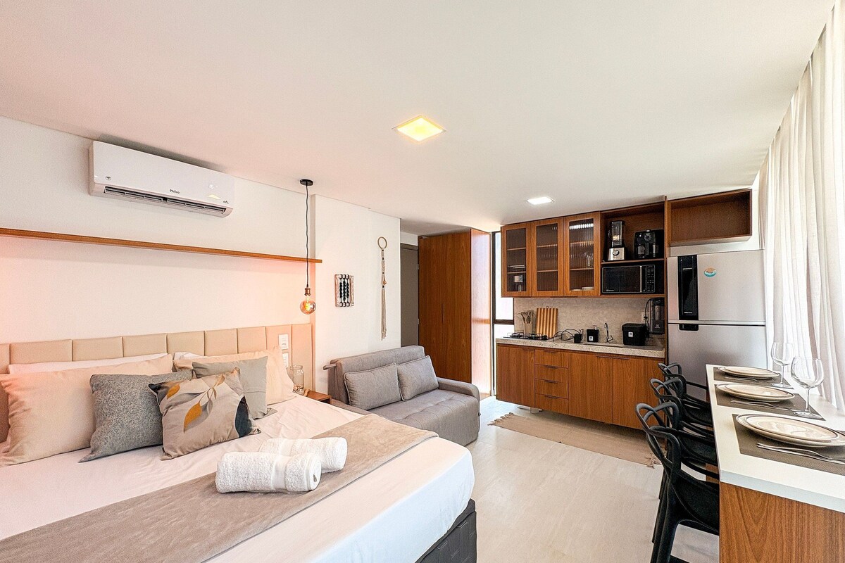 A modern hotel room with a bed, a sofa, a kitchenette, and a dining area.