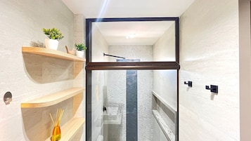 Un baño moderno con cabina de ducha de vidrio, estantes de madera y una planta pequeña.