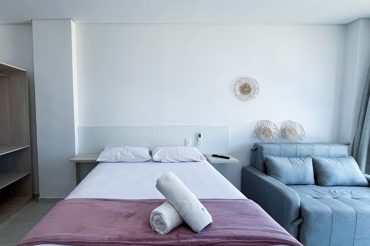 A modern hotel room with a bed, a seating area, and a wardrobe.