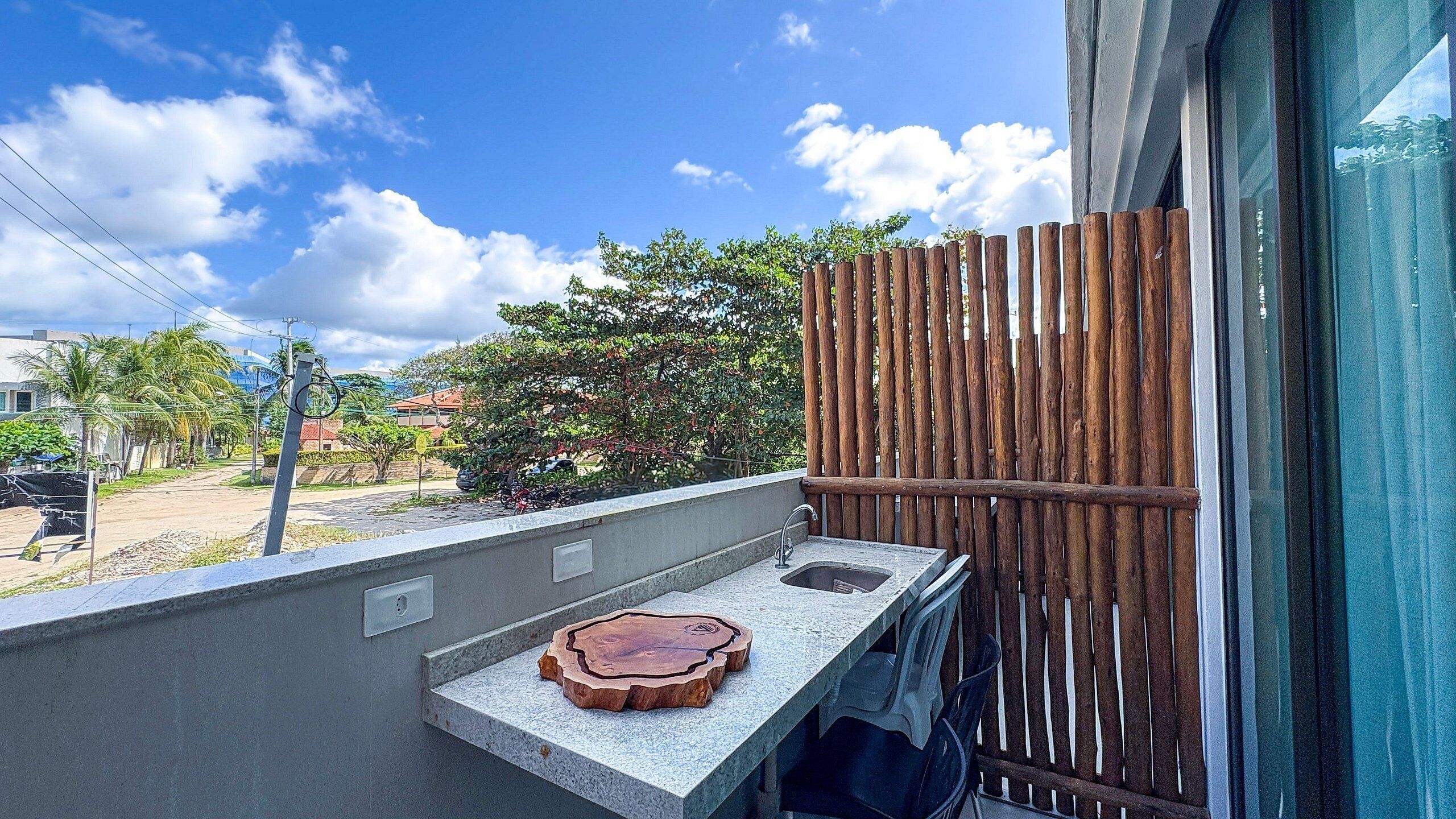 A balcony with a small sink and a wooden tray, overlooking a residential area with trees and a clear sky.