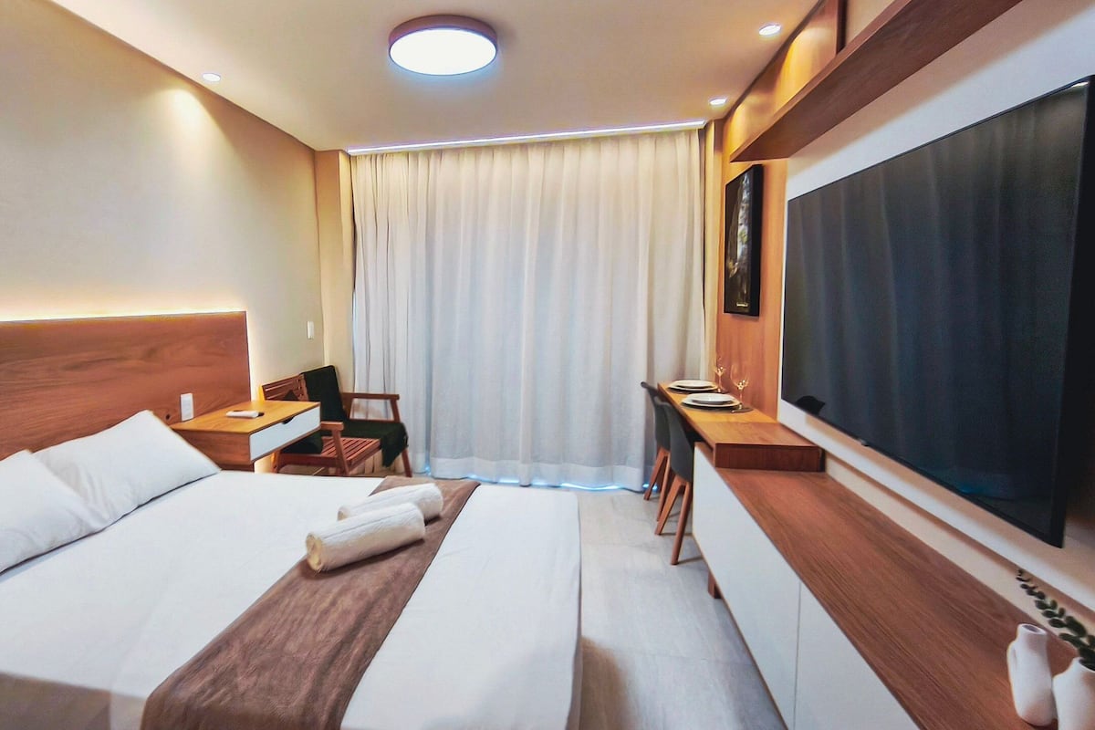 Habitación de hotel con cama, mesitas de noche, escritorio, silla, televisión y ventana con cortinas.
