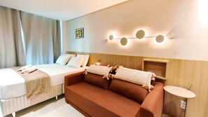 A hotel room with a bed, a sofa, a bedside table, and a wall-mounted light fixture.