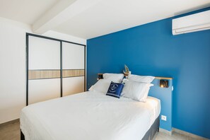 A bedroom with a bed, a nightstand, a wall-mounted air conditioner, and a blue accent wall. - Flat with sea view (Saint Pierre)