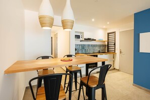 A dining area with a wooden table and black chairs, a kitchen in the background, and a blue accent wall. - Flat with sea view (Saint Pierre)