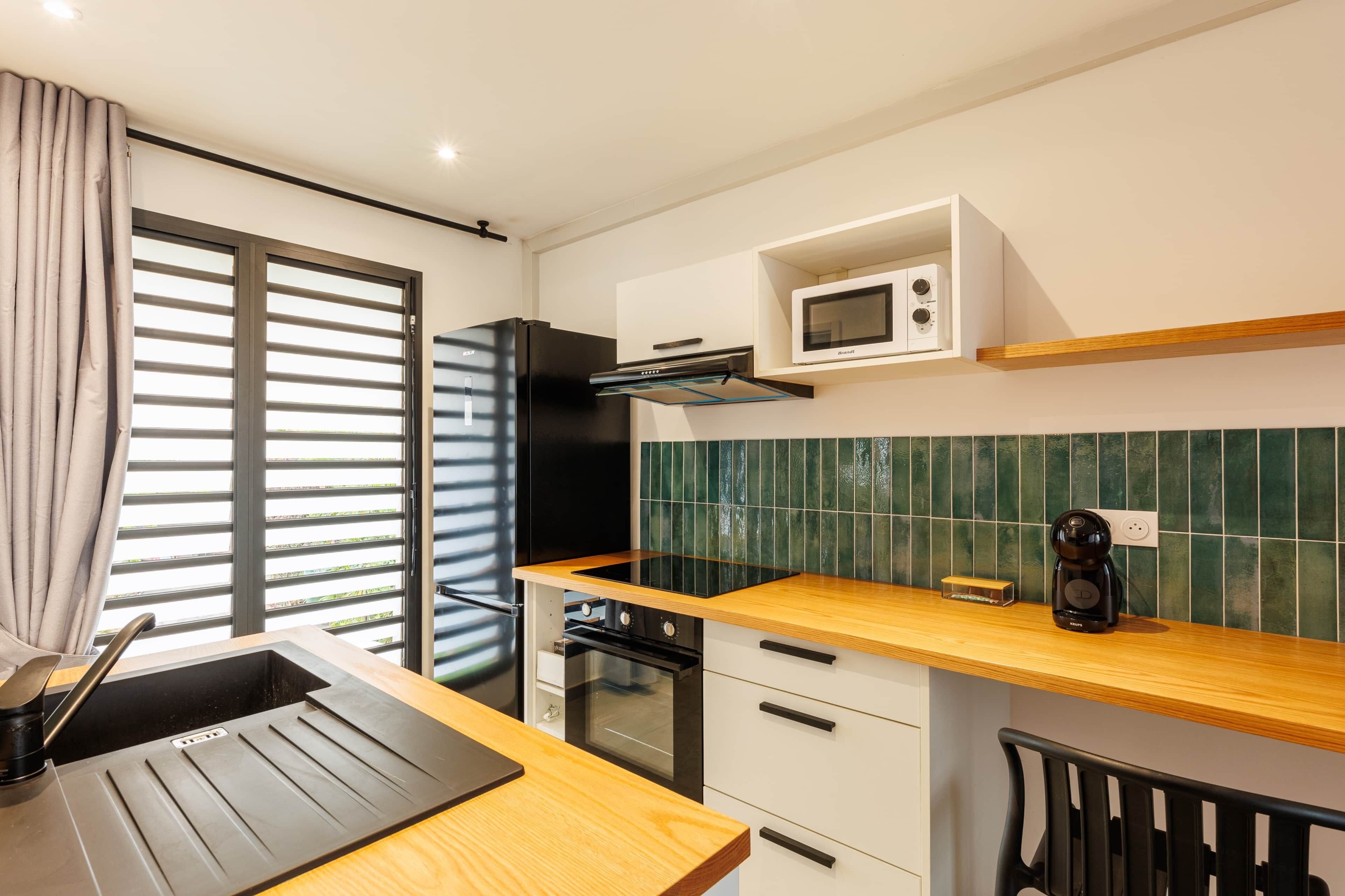 Une cuisine moderne avec un réfrigérateur noir, un four encastré, un micro-ondes et un plan de travail en bois.
