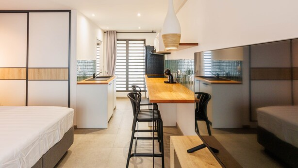 Habitació d'hotel moderna amb llit, escriptori, cadira i petita cuina.