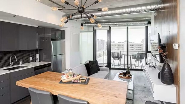 A modern kitchen with a wooden island, stainless steel appliances, and a unique ceiling light fixture. - Modern High-Rise Condo | 2 Bed | 1 Bath | (Winnipeg)