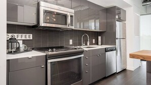 A modern kitchen with stainless steel appliances, a coffee maker, and a wooden table. - Modern High-Rise Condo | 2 Bed | 1 Bath | (Winnipeg)