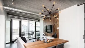 A modern kitchen with a wooden table, grey chairs, a TV mounted on the wall, and a large window with a city view. - Modern High-Rise Condo | 2 Bed | 1 Bath | (Winnipeg)