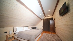 A bedroom with a sloped ceiling, wooden walls, a bed, a nightstand, a TV, and a door. - Maru house (Dilijan)
