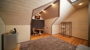 A loft-style room with a sloped ceiling, wooden walls, a small dining table with chairs, a gray refrigerator, and a large window. - Maru house (Dilijan)