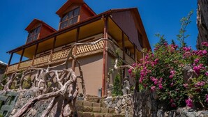 A two-story building with a balcony, stone steps, and pink flowering plants. - Maru house (Dilijan)
