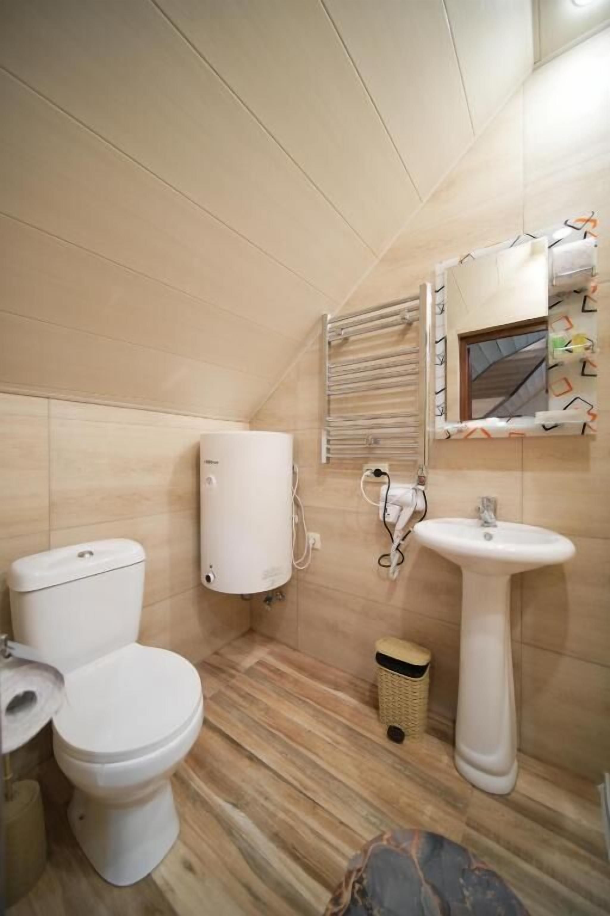 A small bathroom with a toilet, a wall-mounted water heater, a sink, and a window with blinds.