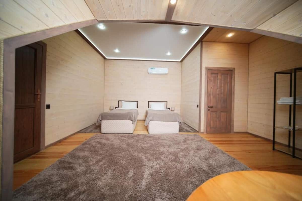 A room with two beds, a ceiling light, and wooden walls.