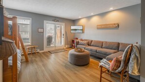 Una sala de estar con un sofá, un reposapiés y una silla con una manta.