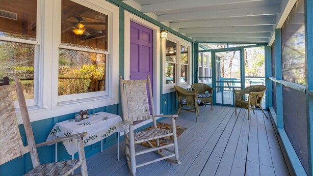 A covered porch with wicker chairs, a table with a tablecloth, and a purple door. - Charming 2-bedroom cottage near Highlands and attractions (Scaly Mountain)