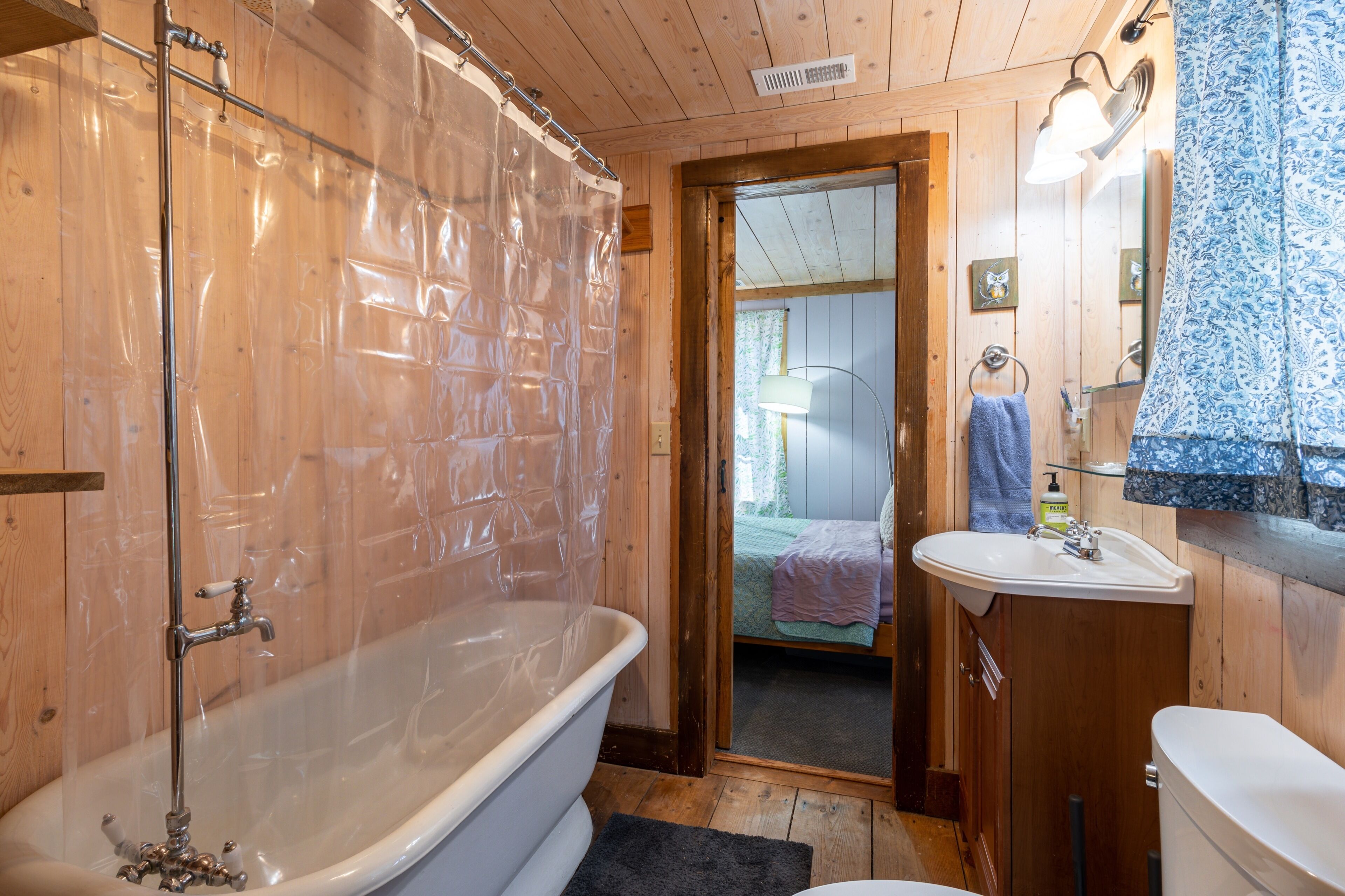Un interior de madera con una bañera, un lavamanos y una puerta que da a un dormitorio.