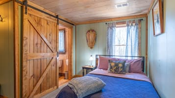 A bedroom with a bed, pillows, a nightstand, a lamp, a wooden door, and a window with curtains.