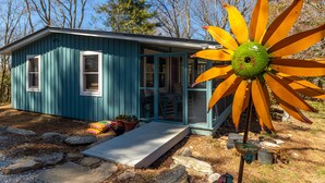 A small blue cabin with a glass door, a concrete step, and a large yellow flower decoration. - Charming 2-bedroom cottage near Highlands and attractions (Scaly Mountain)