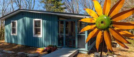 A small blue cabin with a glass door, a concrete step, and a large yellow flower decoration.