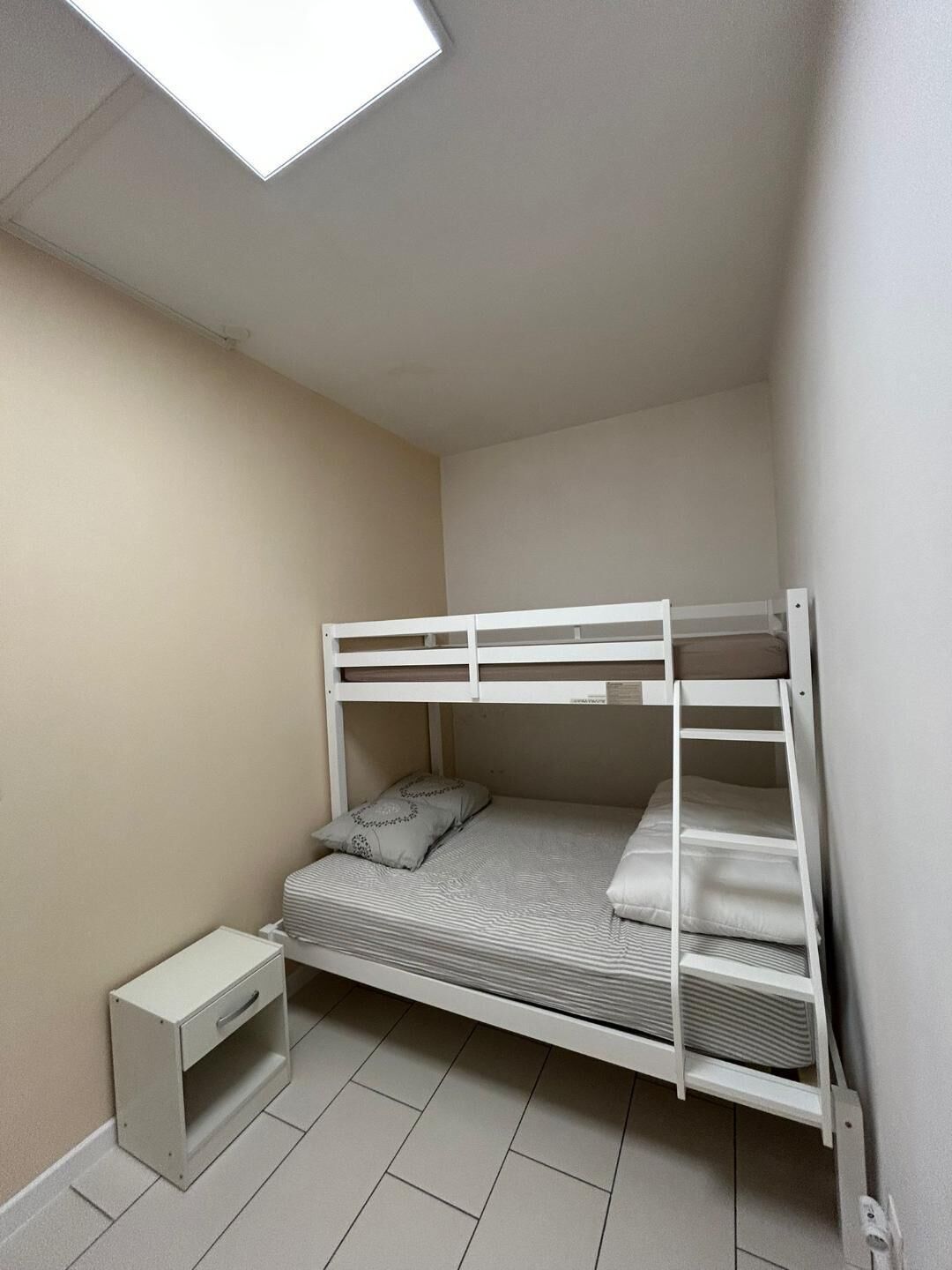 A bunk bed in a small room with a single bedside table and a skylight above.