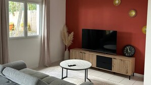 A living room with a grey sofa, a white coffee table, a TV on a wooden cabinet, and a red accent wall. - 2-bedroom apartment with private pool (Saint-Paul)