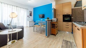Una sala de estar moderna con sofá, una mesa de comedor y una cocina con armarios de madera y televisor.