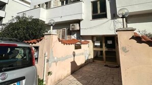 Un edificio moderno de varios pisos con entrada protegida por una reja, un coche estacionado y cielo despejado.