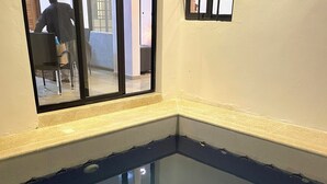 Una piscina en esquina con agua cristalina, una ventana con vidrio reforzado y una persona visible a través de la ventana.