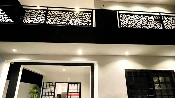 Un edificio moderno de dos plantas, con un balcón y barandilla decorativa, y una puerta con diseño de cuadrícula.