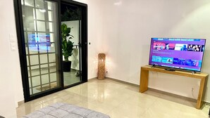 Una sala de estar con una televisión sobre un mueble de madera, un sofá gris, un vidrio y una planta en maceta.
