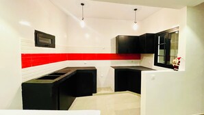 Una cocina compacta con paredes blancas, una pared de acento roja, armarios negros y una pequeña ventana con vistas.