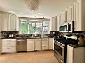A modern kitchen with white cabinets, a large window, and stainless steel appliances.