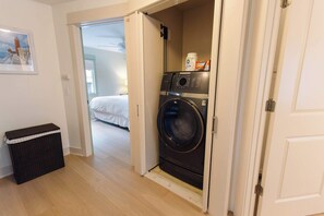 Une buanderie équipée d’un lave-linge, d’un panier à linge et d’une porte donnant sur une chambre.