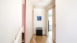 A hallway with a black trash bin, a framed picture on the wall, and a white door at the end. - Harborside Grand Haven - Walk to Lake Michigan (Grand Haven)