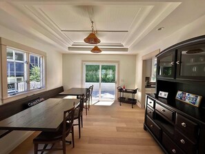A modern kitchen with a dining area, large windows, and a view of greenery.