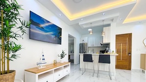 Een moderne keuken met een marmeren aanrecht, een houten eettafel met twee stoelen, en een grote flatscreen televisie aan de muur.