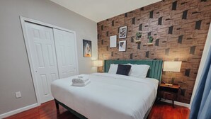 A neatly made bed with a green headboard, a pair of bedside tables with lamps, a patterned wallpaper, and a door with a white frame. - Element / King Bed / Elevator / Adjustable Desk (Philadelphia)