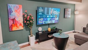 A modern living room with a flat-screen TV, abstract paintings, a potted plant, a round coffee table, and a grey sofa. - Element / King Bed / Elevator / Adjustable Desk (Philadelphia)