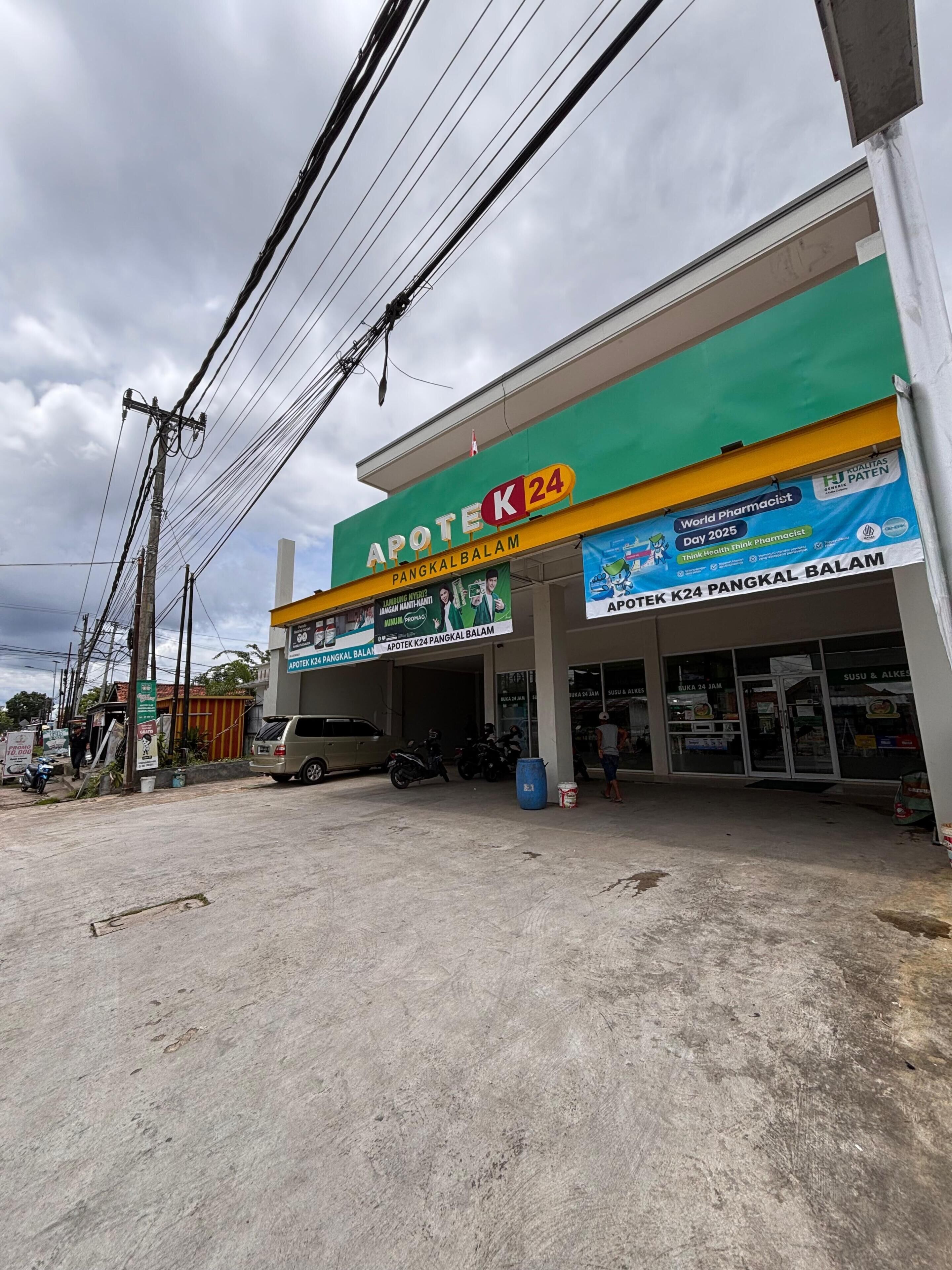 Una farmacia con fachada verde y amarilla, varios letreros y un cielo despejado.
